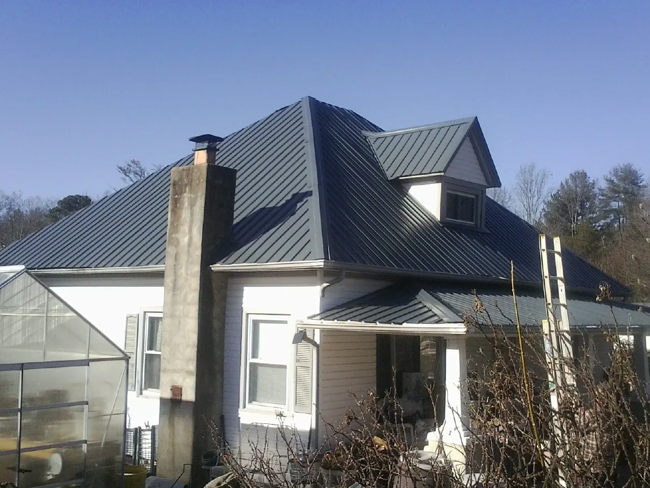 Dark blue standing seam metal roof on a white farmhouse with dormer — Slate & Tile Roof Repair by Roofing Brothers in Wheatland