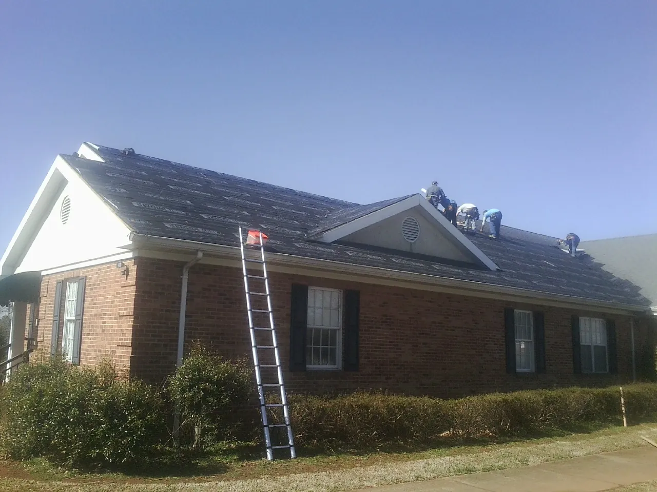 Crew tearing shingles off a brick ranch roof with a ladder set — Metal Roof Repair work by our crew in Wheatland