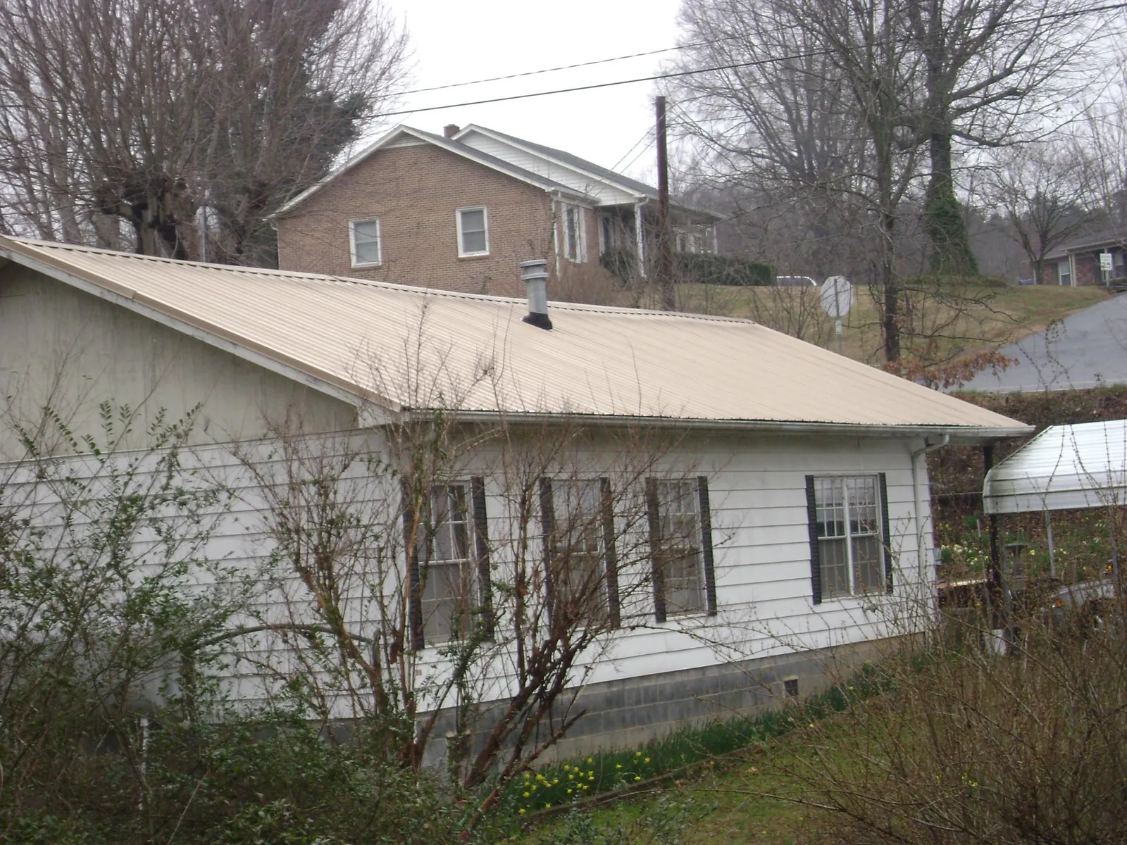 Tan metal roof on a white sided house set into a hillside — Commercial Roofing by Roofing Brothers in Wheatland